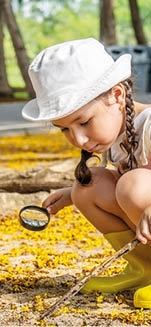 Image of cute girl exploring the nature with magnifying glass outdoors, Child playing in the forest with magnifying glass  Curious kid searching with magnifier on the grass in the park